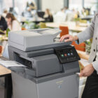 Office employee using a Sharp multifunction printer with a touchscreen display in a modern office setting