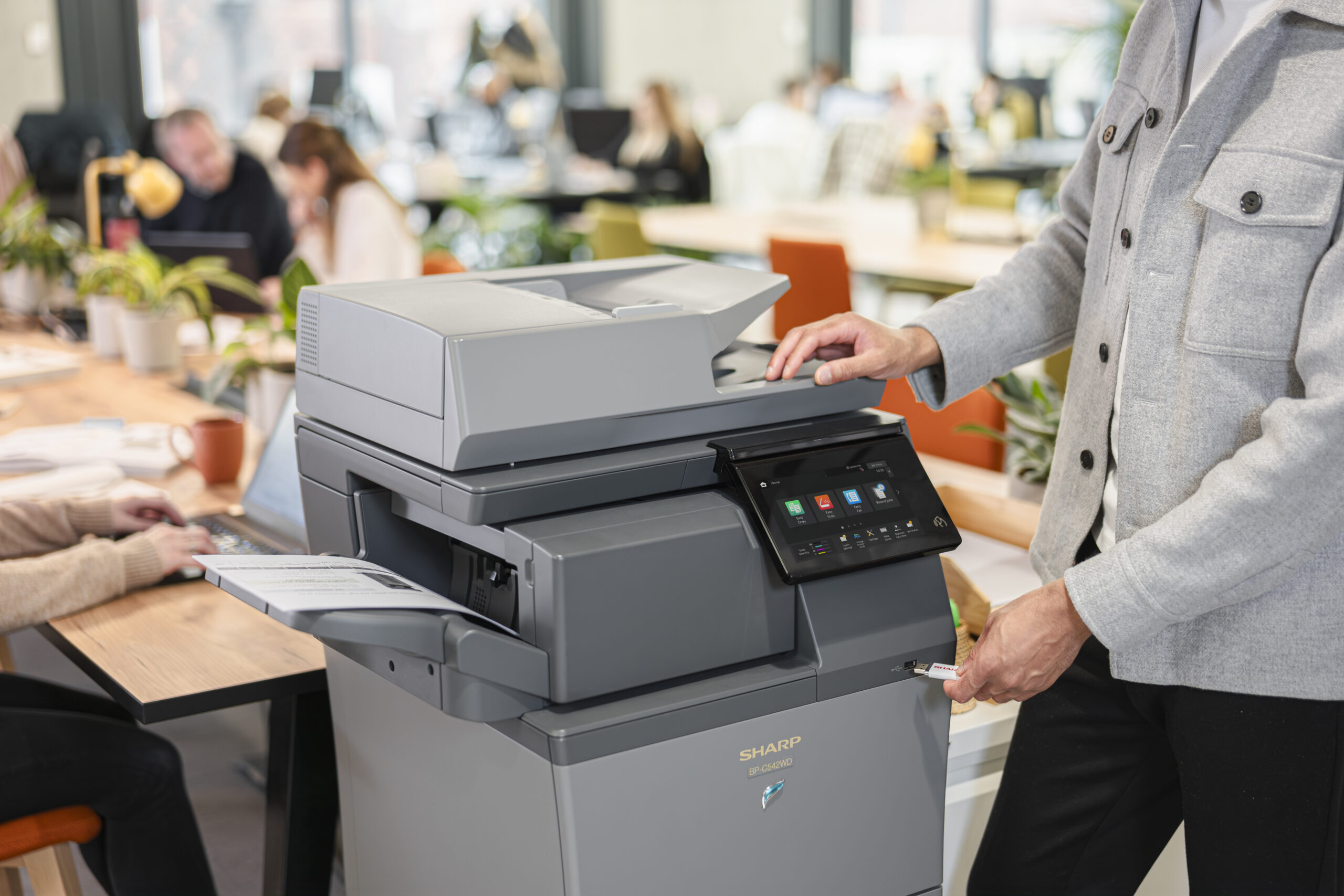 Office employee using a Sharp multifunction printer with a touchscreen display in a modern office setting